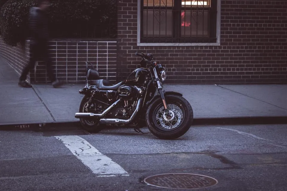 Black motorbike parked at the kerb beside a brick building